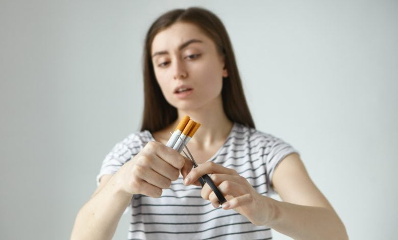 mujer sosteniendo varios cigarrillos en su mano, mientras los corta con una tijera