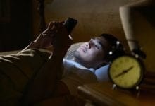 joven en cama con adicción al celular