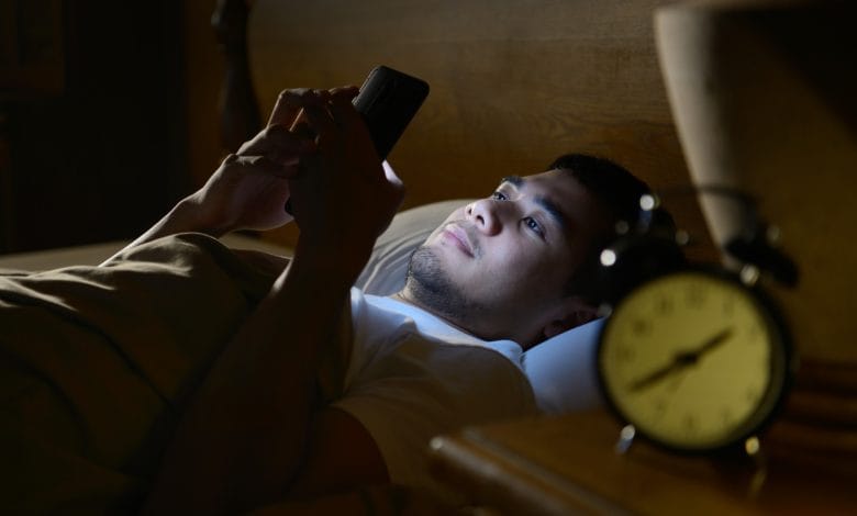 joven en cama con adicción al celular